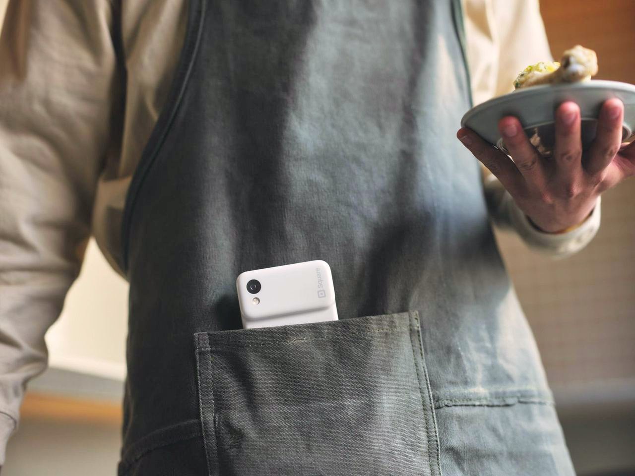 A Square Handheld in a server apron pocket while the server carries a plate