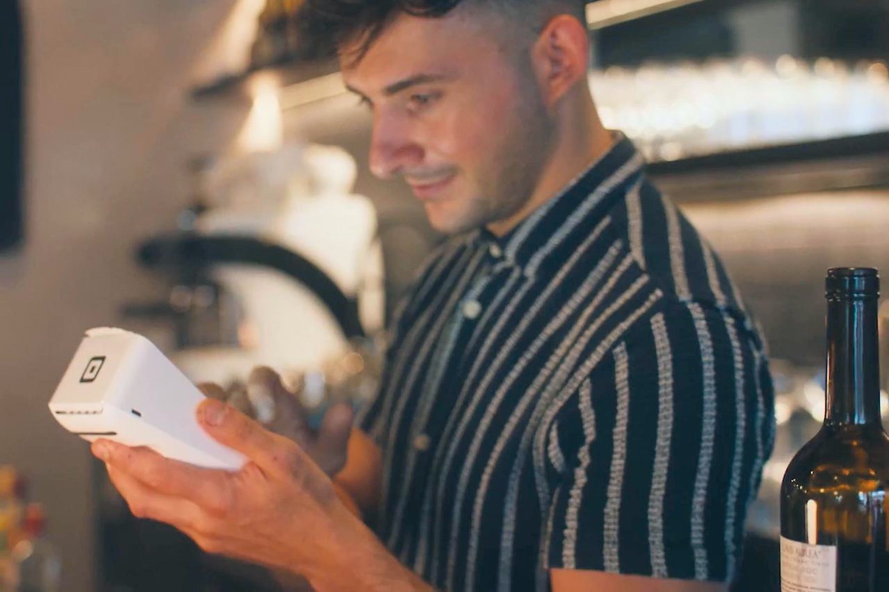 A bartender checking an order on a Square Handheld behind the bar