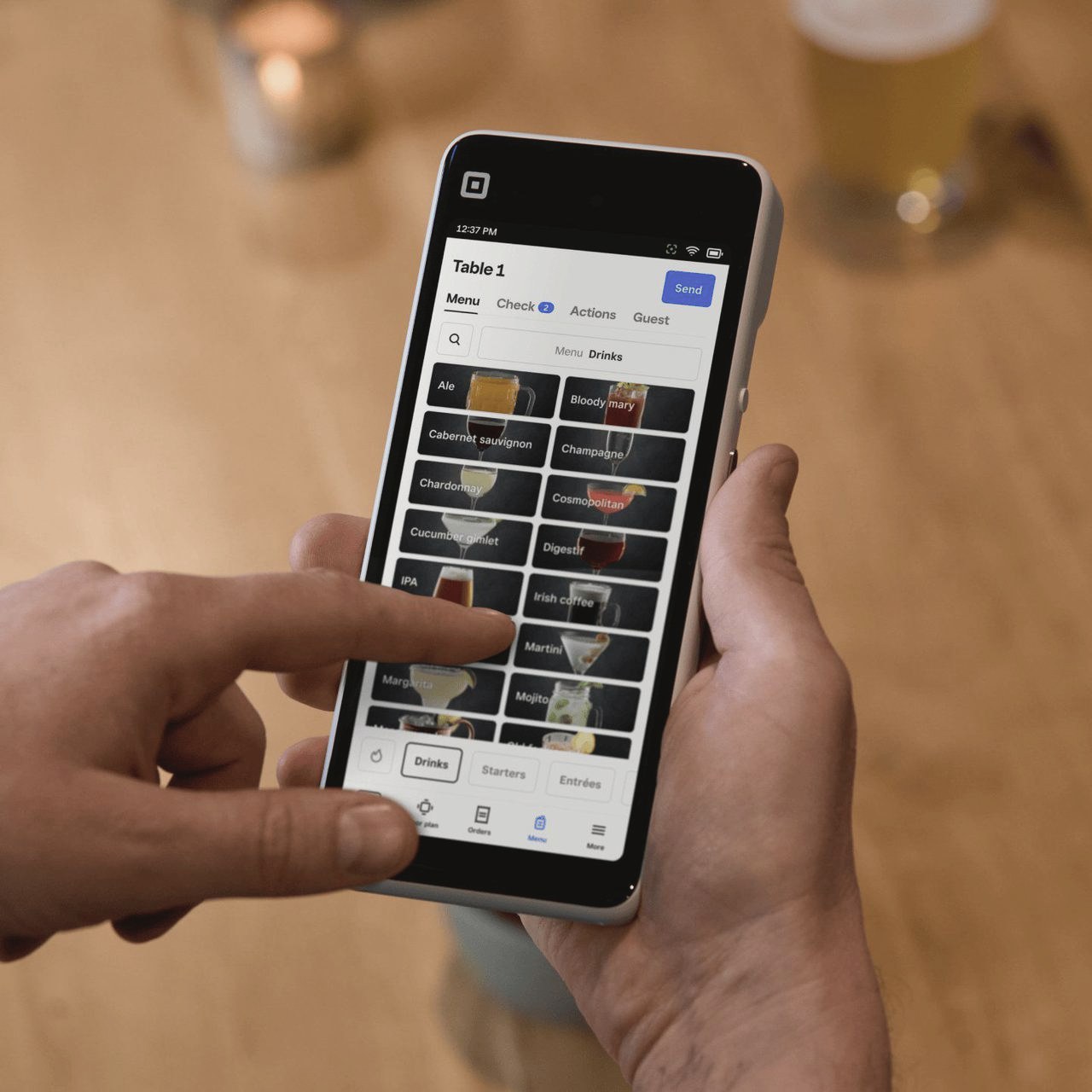 Hands entering a drinks order on a Square Handheld at a bar table