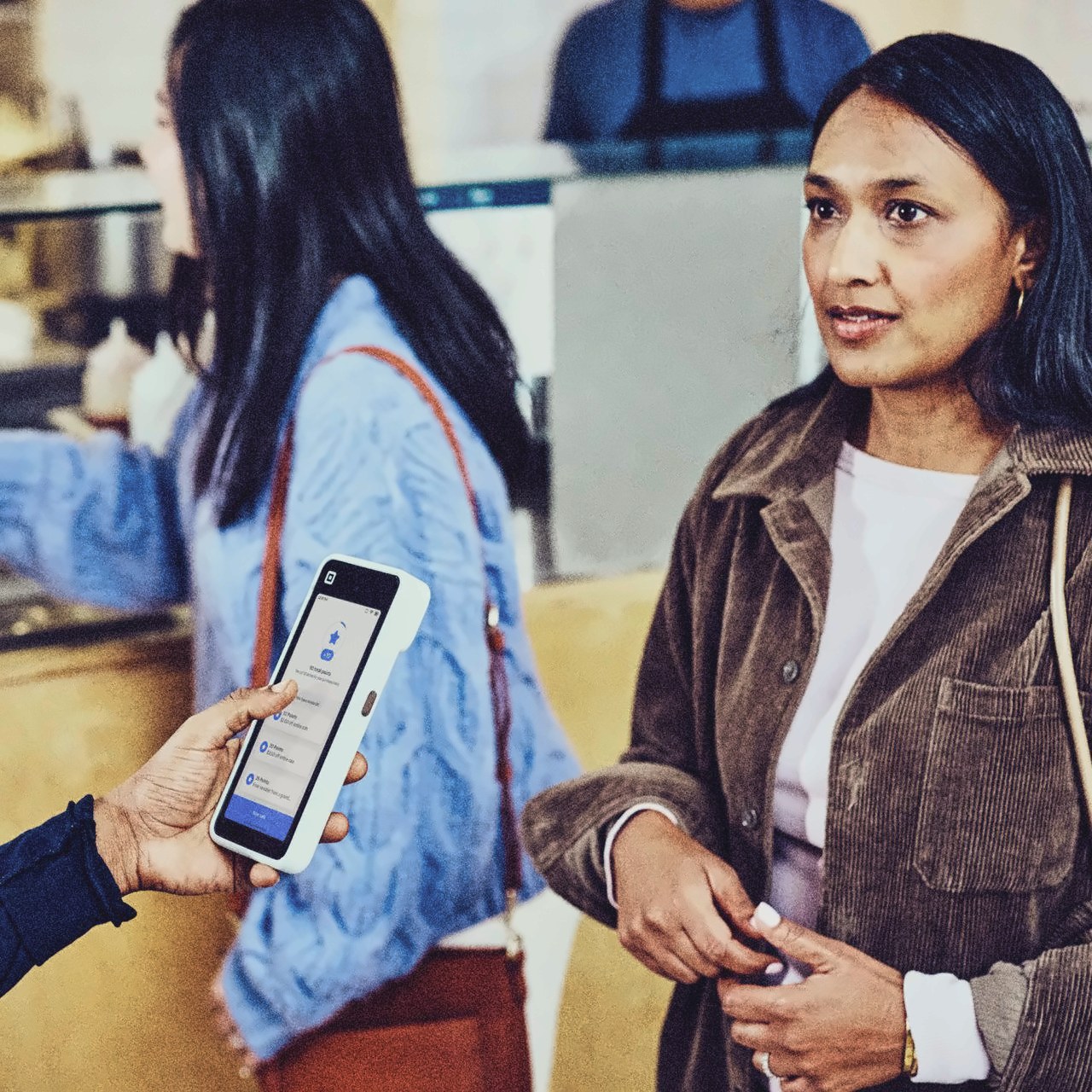 A staff member showing a guest in line the loyalty screen on a Square Handheld
