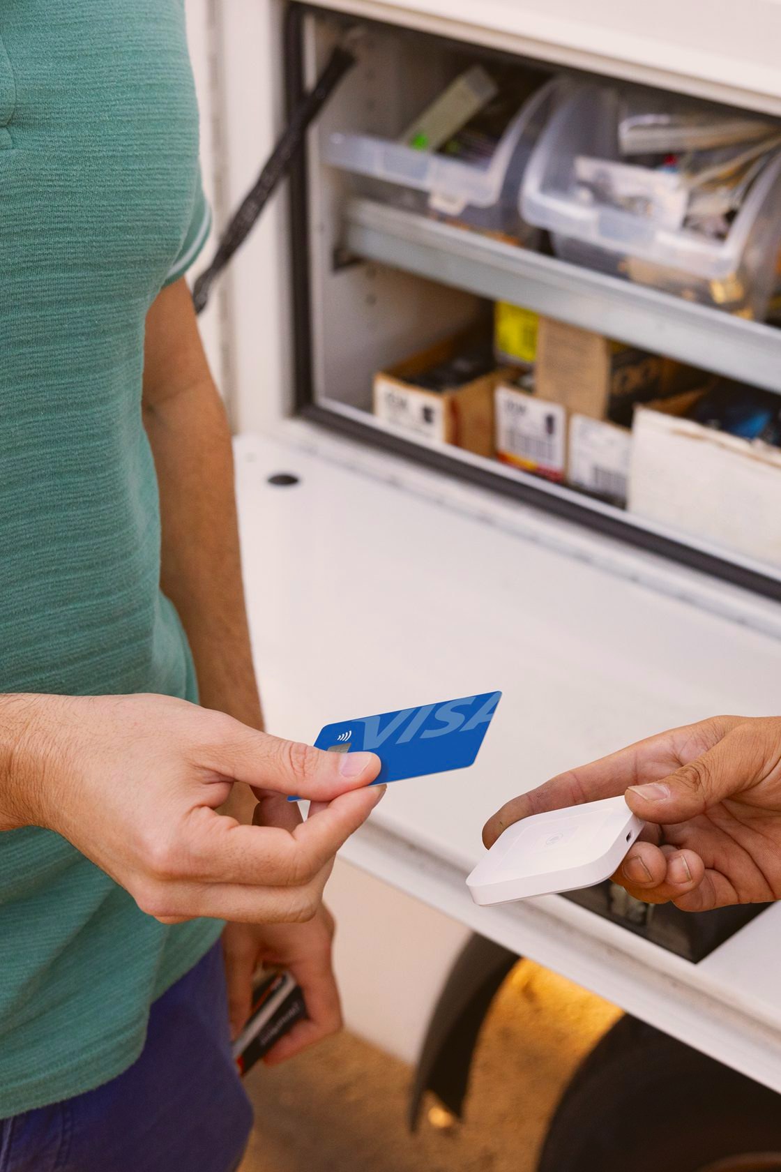 A contractor takes a card payment on a Square Reader at the back of a work van