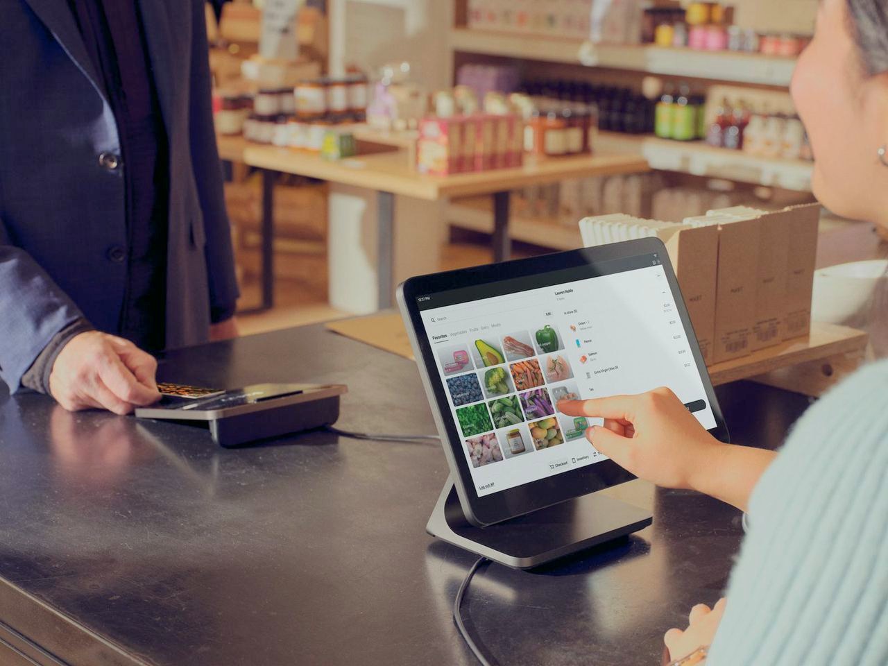 A cashier ringing up produce on a Square Register while the customer pays at the customer display