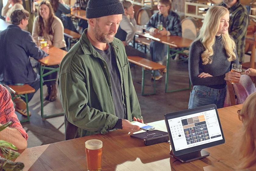 A customer pays by phone at a Square Register (2nd generation) in a busy taproom