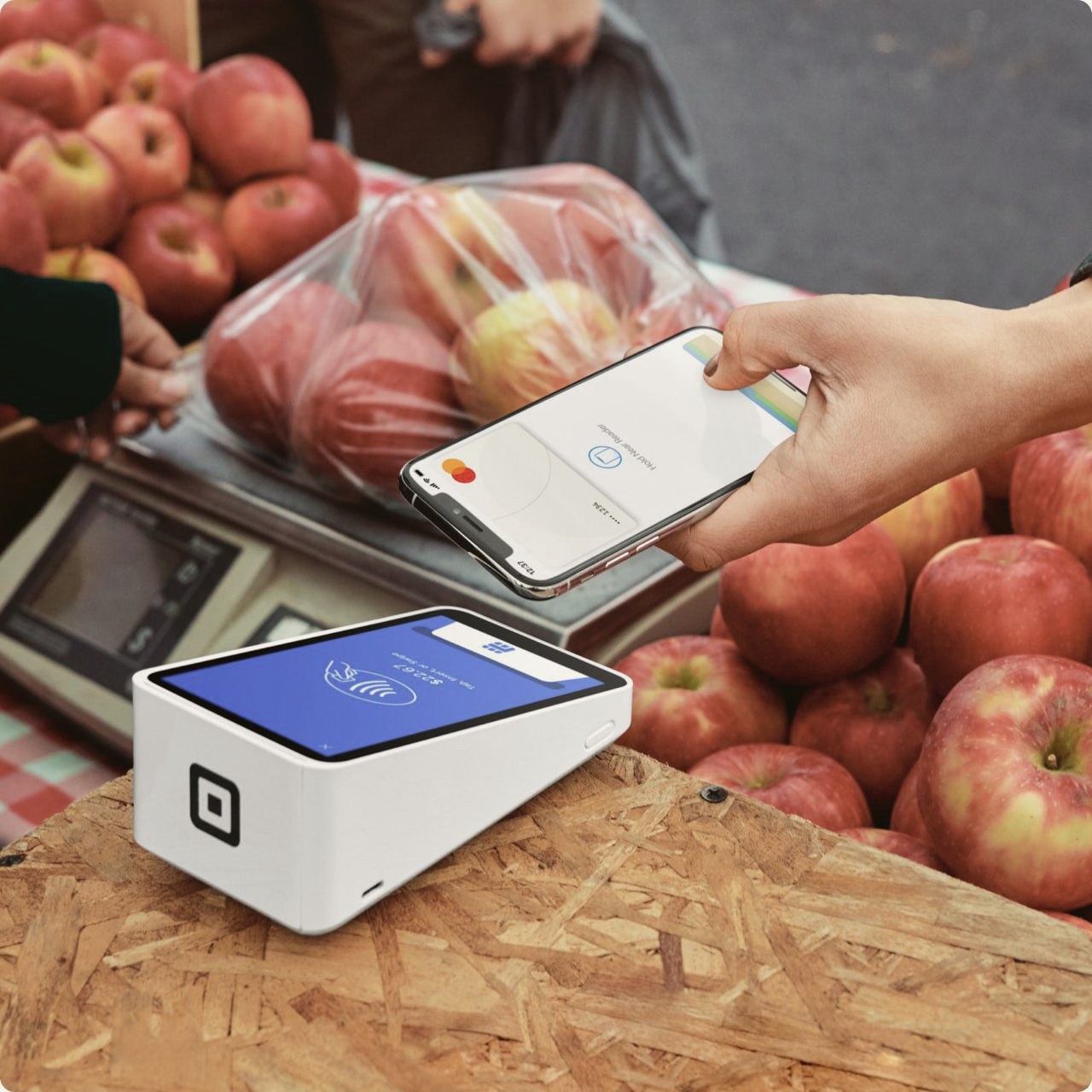 A customer tapping a phone on a Square Terminal at a fruit stand