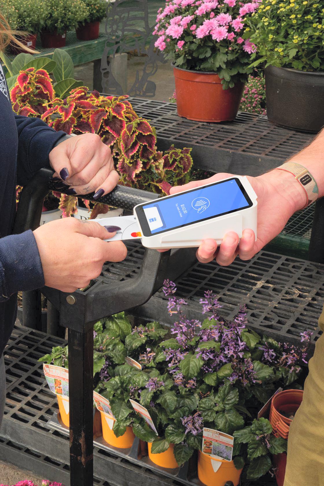 A customer dipping a card into a Square Terminal among flower racks at a garden center